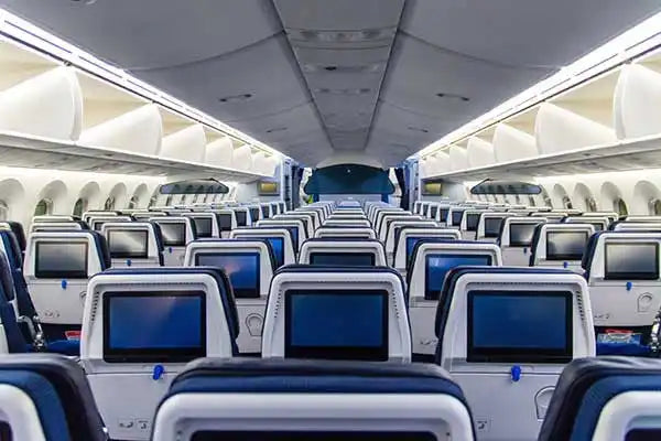 Empty airplane cabin interior with rows of blue and grey seats featuring entertainment screens.