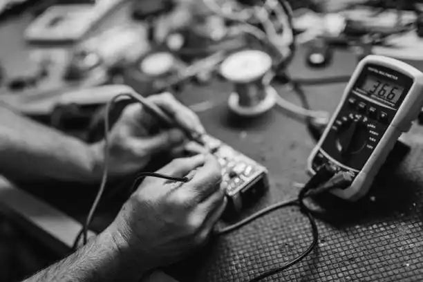 Hands using a multimeter to test an electronic circuit or component.