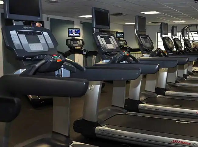 Row of modern treadmills with digital display screens mounted on them.